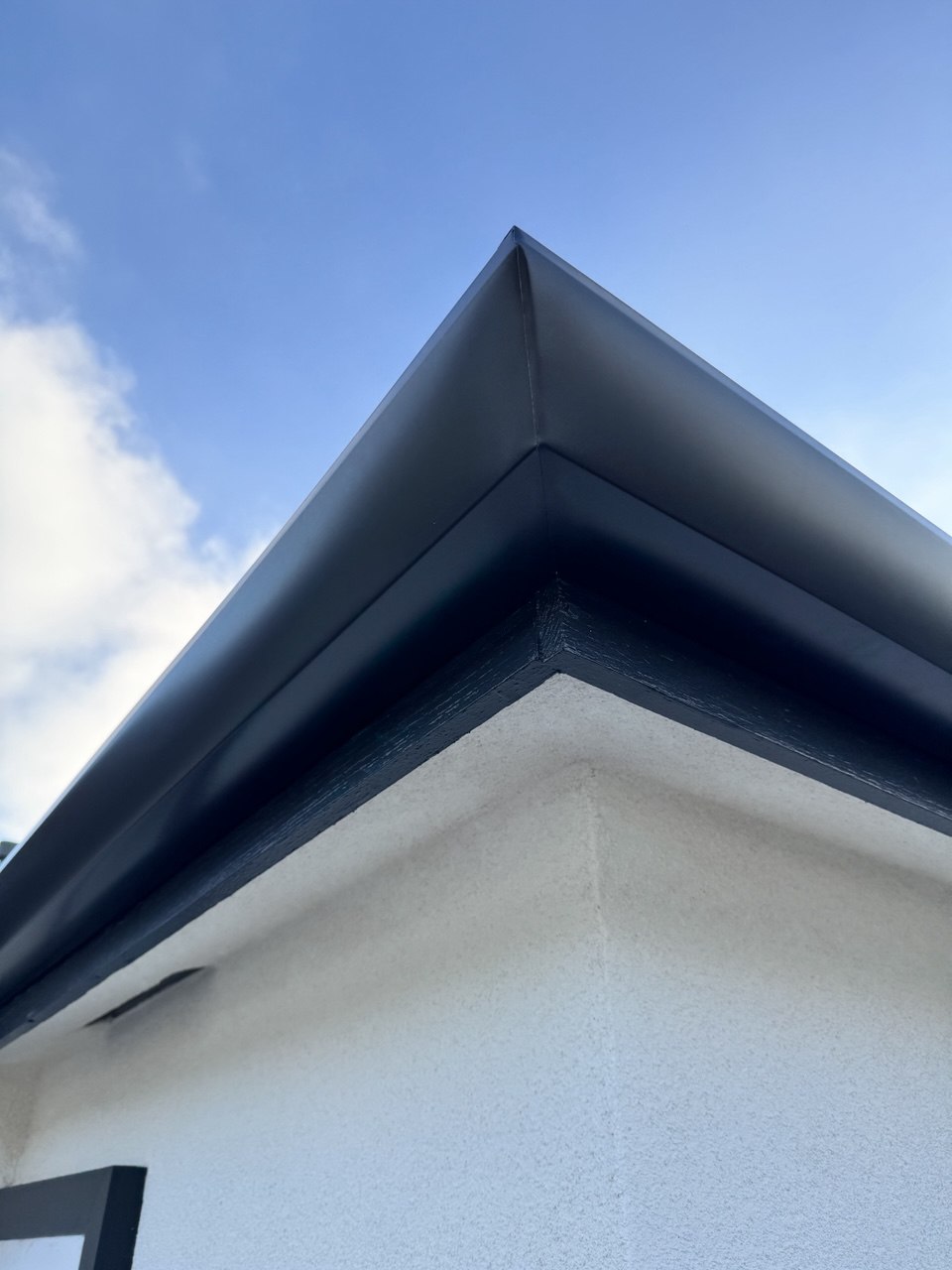 Charcoal seamless gutter corner installation on white stucco home - Flashpoint Builders